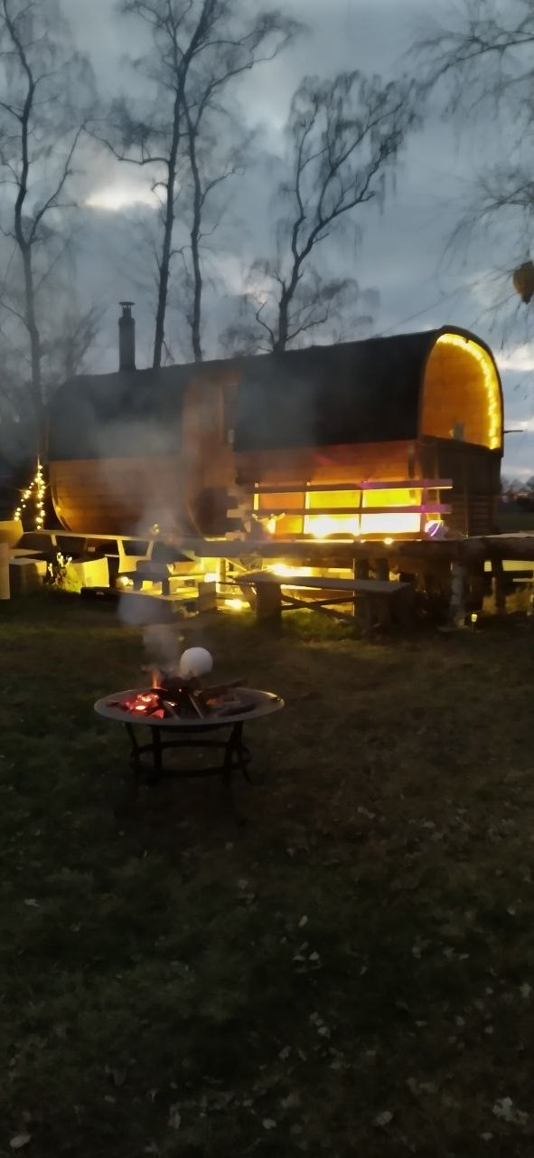 Fasssauna mit Feuerschale in der Dämmerung